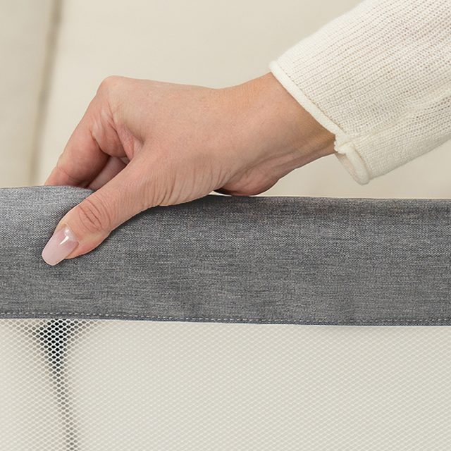 Hand resting on the padded rail and mesh side of a BCOL bassinet